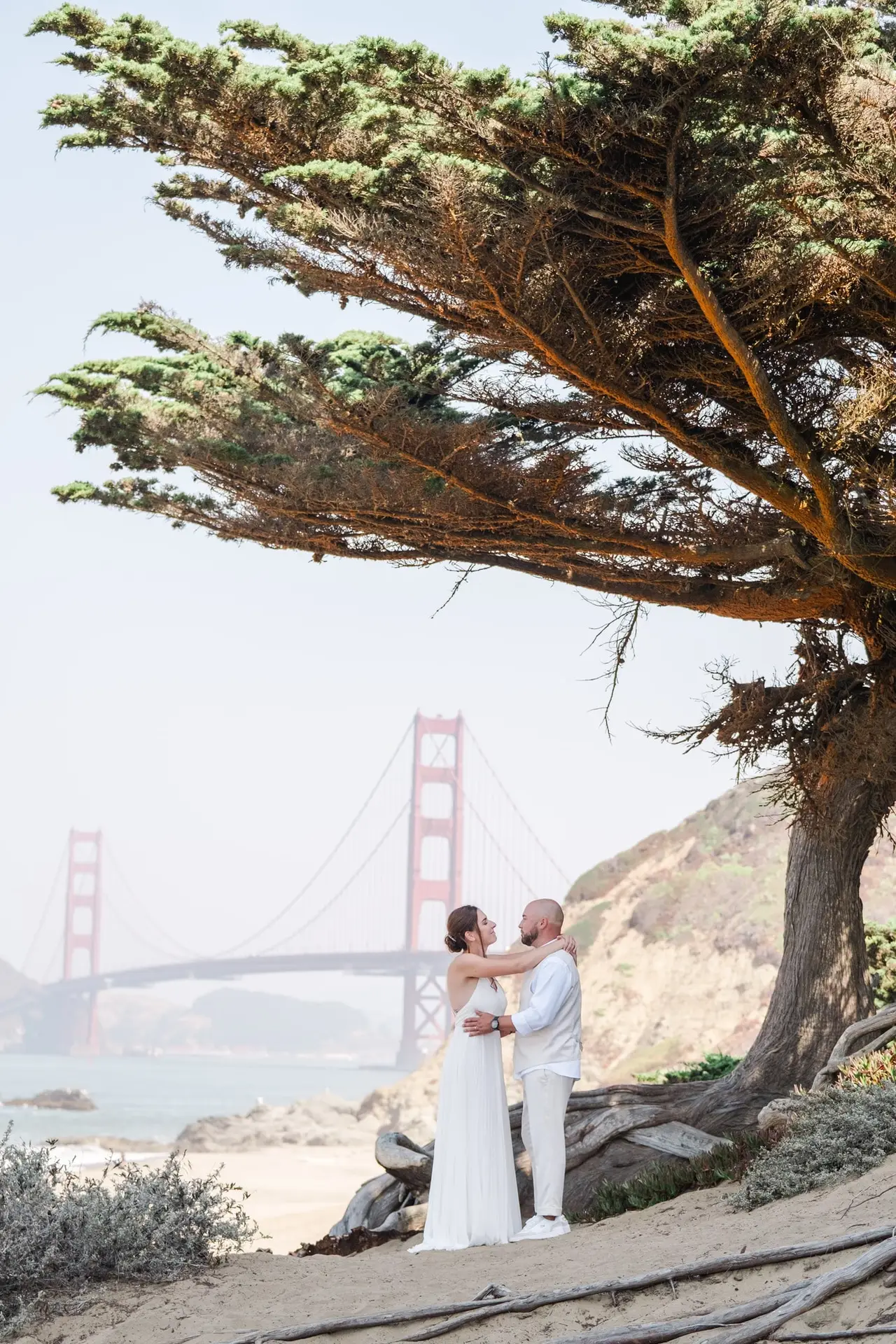 Couple de mariés enlacé sous les arbres avec vue sur le Golden Gate Bridge à San Francisco photographié par Julien Boyer