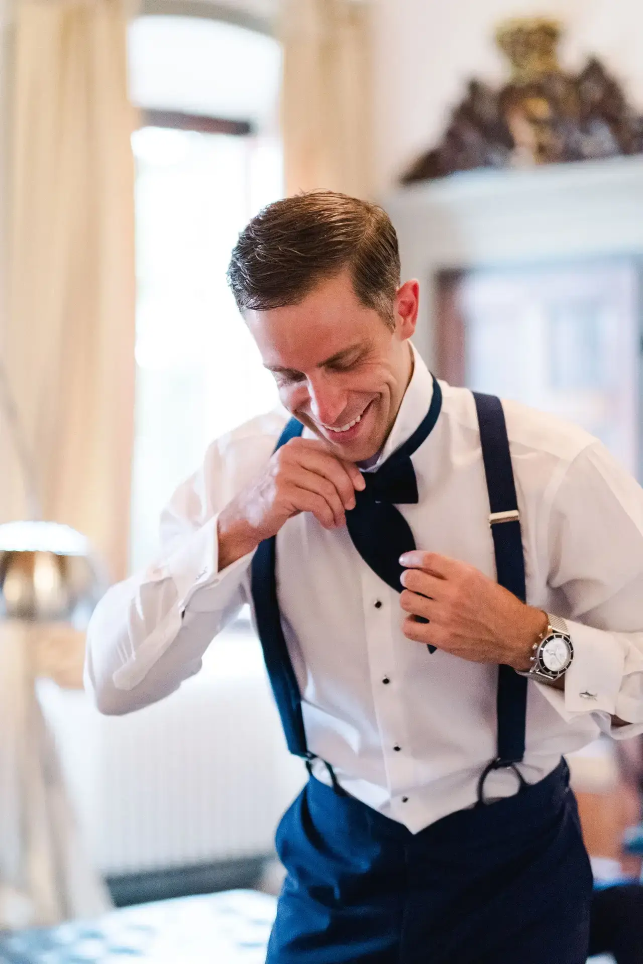 Marié ajustant son nœud papillon et ses bretelles lors des préparatifs dans une villa en Toscane, photo réalisée par Julien Boyer, photographe de mariage de destination.
