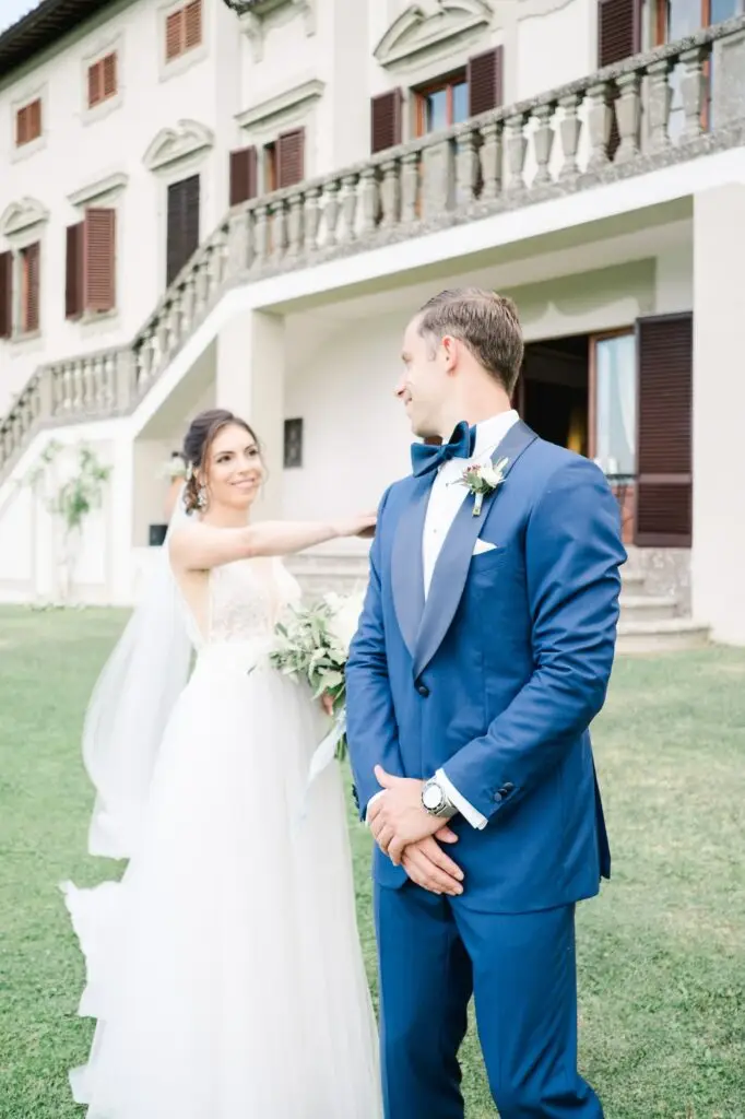 La mariée touche l’épaule du marié lors de leur first look devant la Villa Vistarenni en Toscane, moment fort en émotion photographié par Julien Boyer.