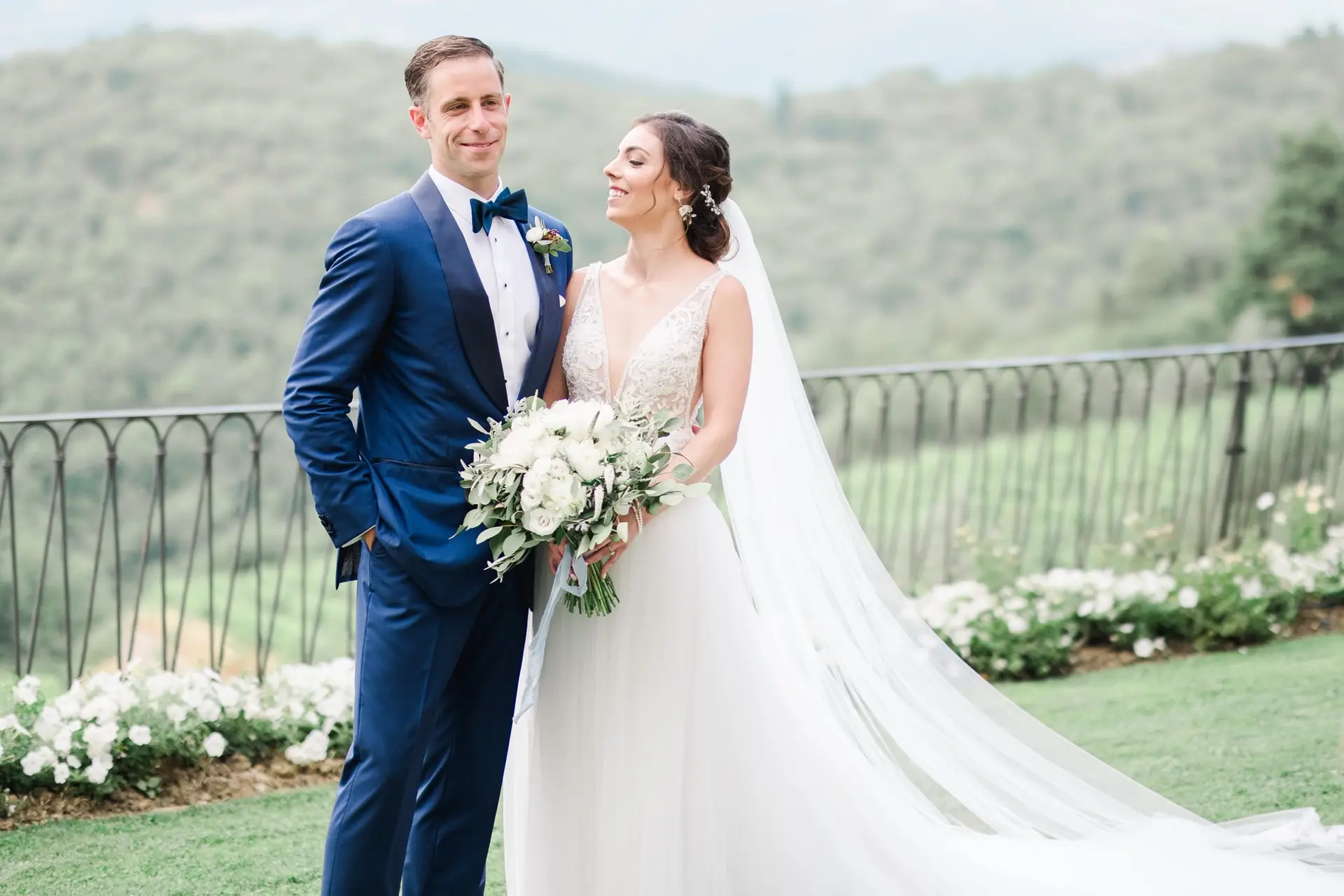 Les mariés posent ensemble avec un bouquet de fleurs blanches et une vue panoramique sur les collines toscanes, mariage de destination en Italie.