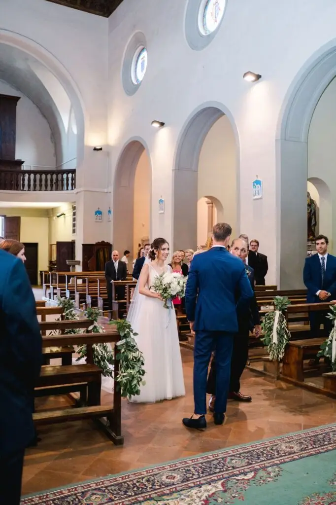 La mariée avance dans l’allée de l’église en Toscane entourée de ses invités, moment solennel d’un mariage de destination.
