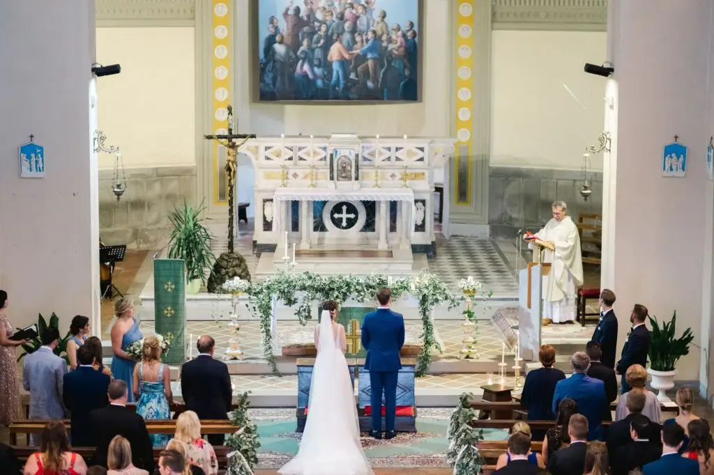 Les mariés debout devant l’autel pendant la cérémonie religieuse en Toscane, entourés de leurs proches dans une église italienne.