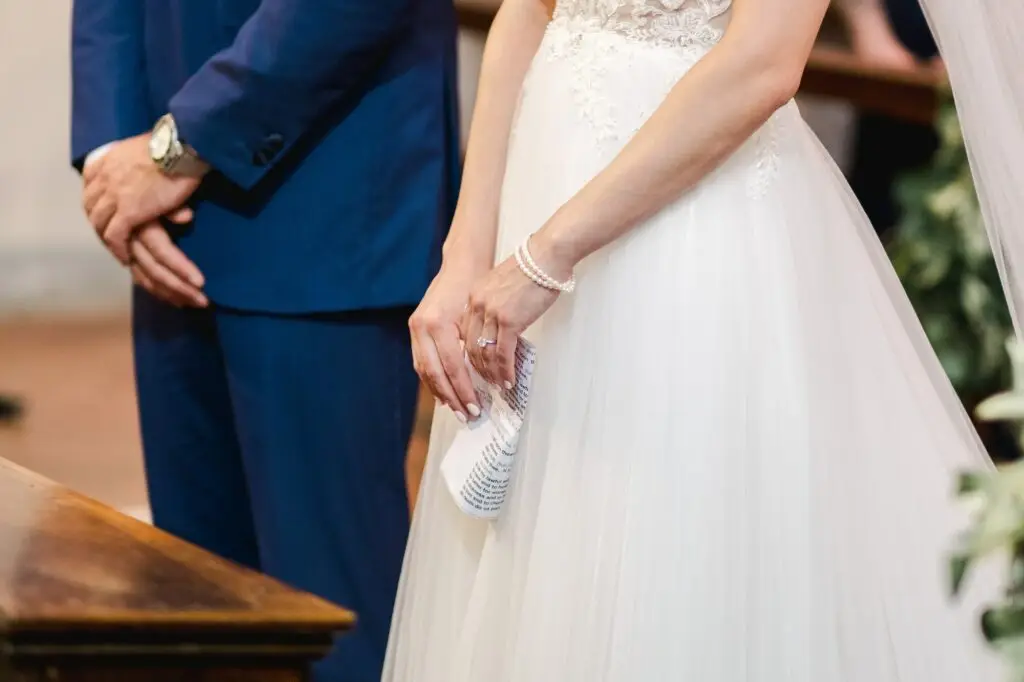 Détail des mains des mariés tenant un livret de cérémonie pendant un mariage religieux en Toscane, photo prise par Julien Boyer, photographe de destination.
