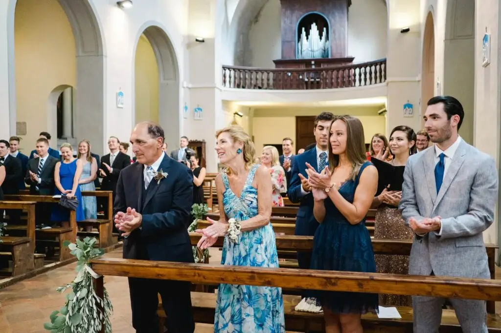Les invités applaudissent avec émotion pendant la cérémonie de mariage dans une église en Toscane, ambiance chaleureuse et authentique.