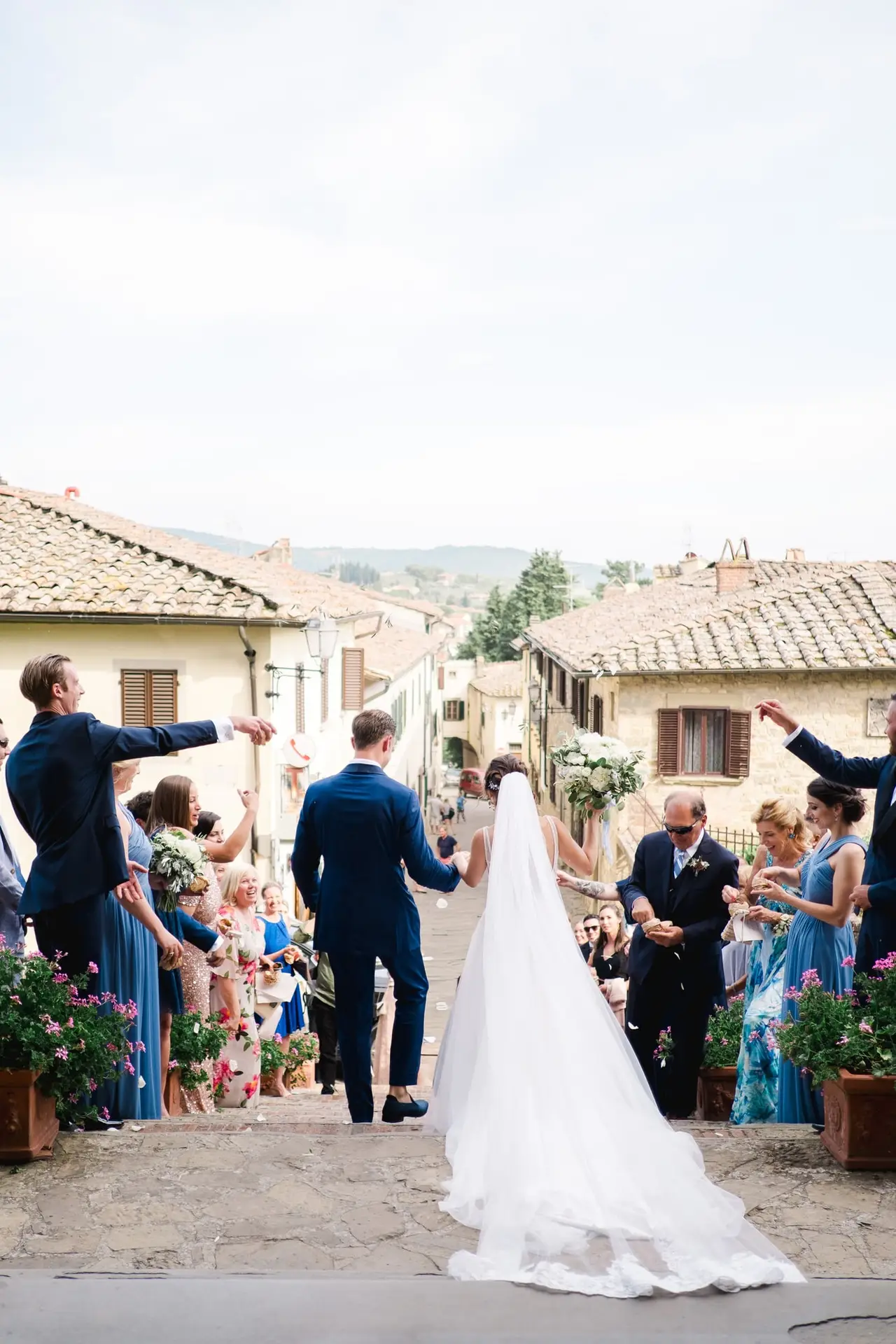 Les mariés quittent la cérémonie entourés de leurs invités dans un village toscan, scène joyeuse d’un mariage de destination photographiée par Julien Boyer.