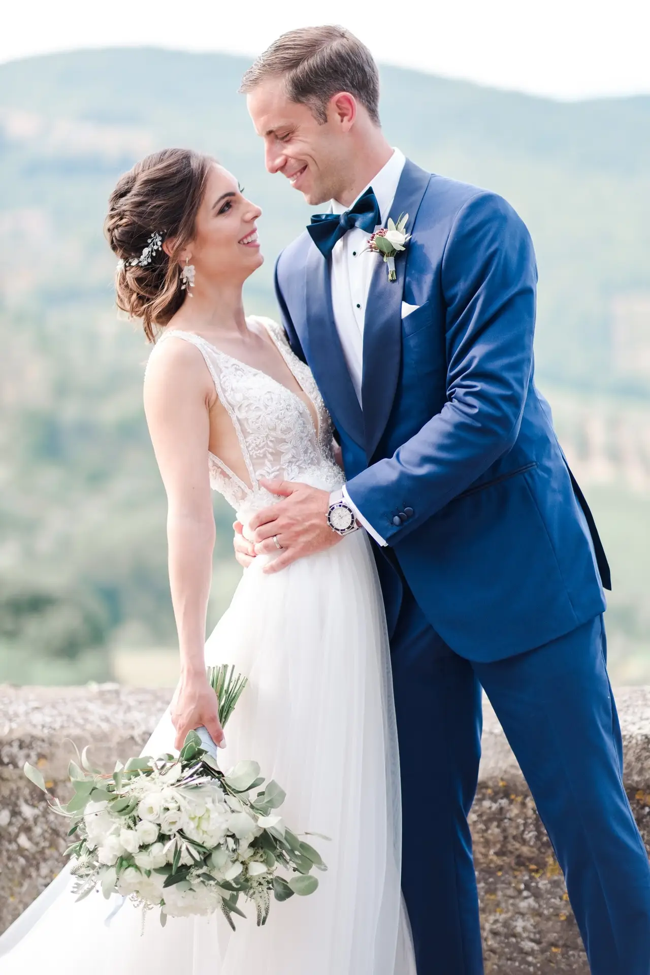 Portrait rapproché des mariés s’enlaçant avec un bouquet de fleurs blanches, séance couple en Toscane lors d’un mariage de destination.
