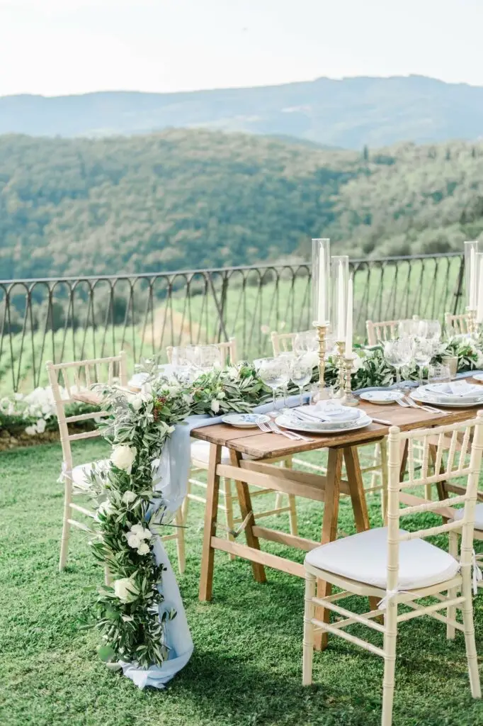 Longue table de réception décorée de bougies et feuillage pour un dîner de mariage élégant en Toscane, ambiance chaleureuse et romantique.