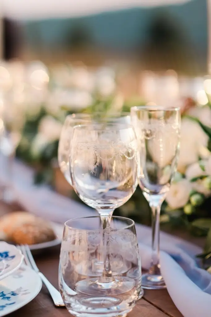 Gros plan sur des verres gravés disposés sur une table de réception lors d’un mariage de destination en Toscane, ambiance raffinée et chaleureuse, photo prise par Julien Boyer, photographe de destination.