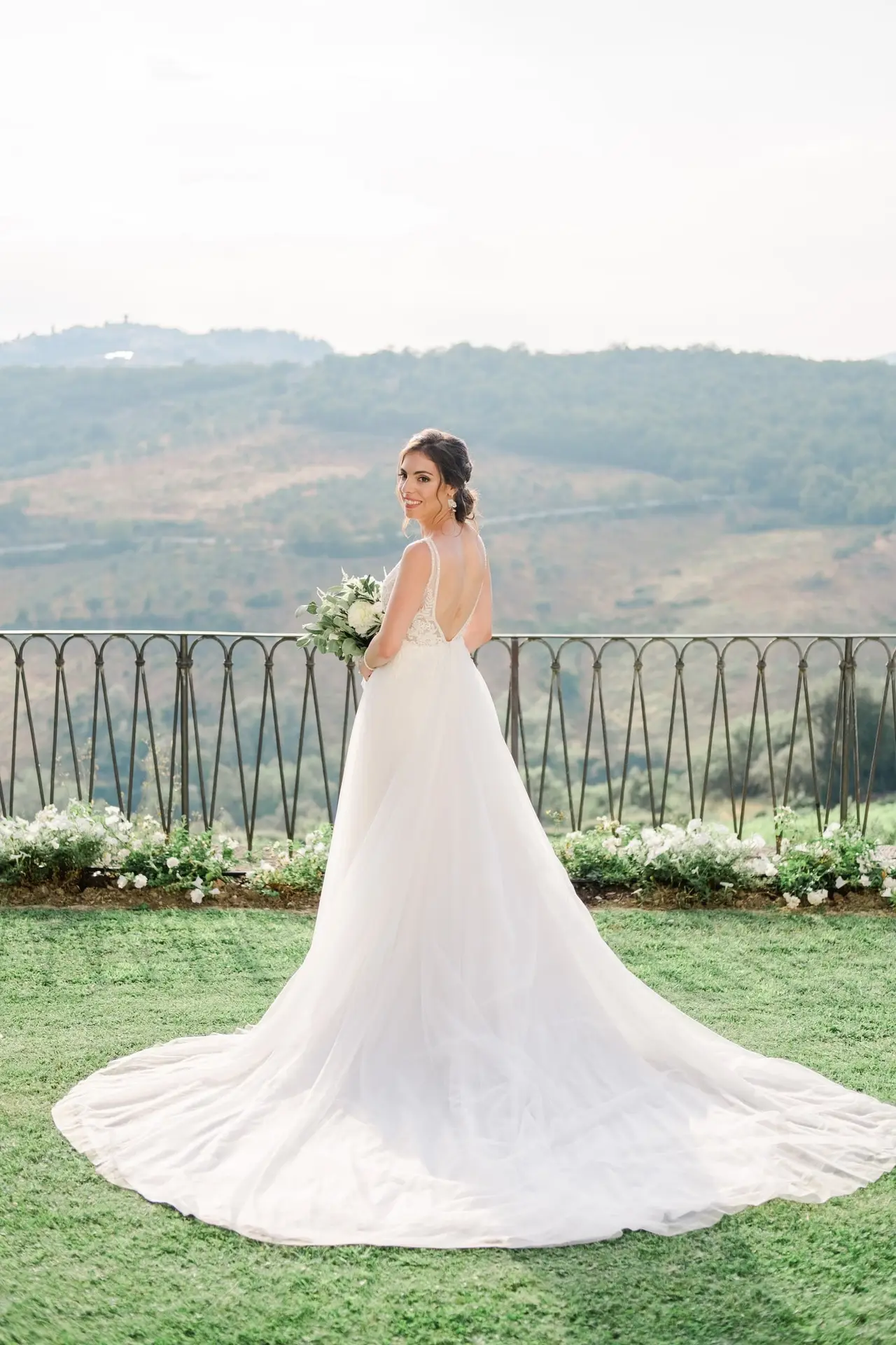 Mariée en robe de dentelle tenant son bouquet face aux collines de Toscane à la Villa Vistarenni, photographie de mariage élégante et lumineuse.