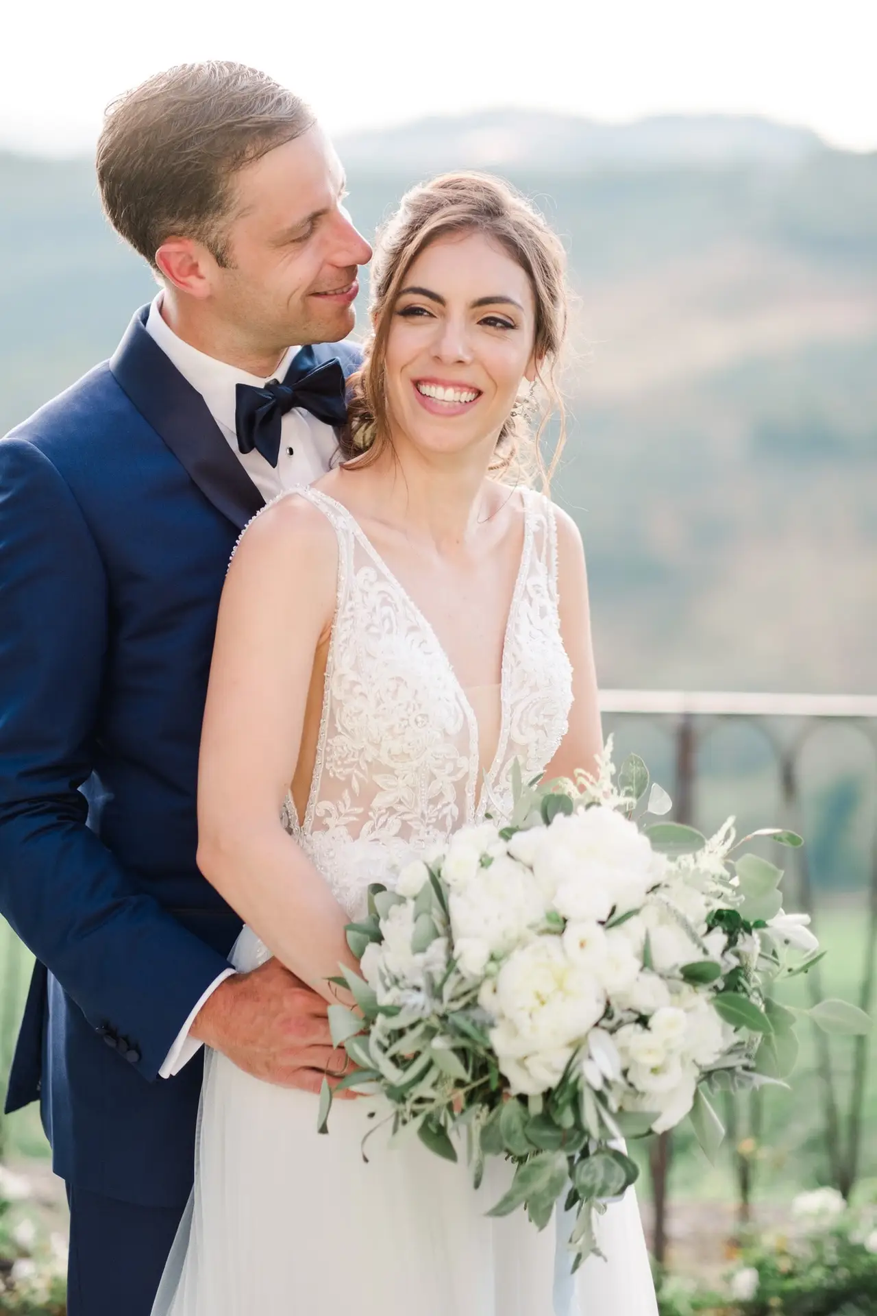 Les mariés enlacés sourient avec vue sur les paysages toscans, séance couple lors d’un mariage à la Villa Vistarenni, photo prise par Julien Boyer.