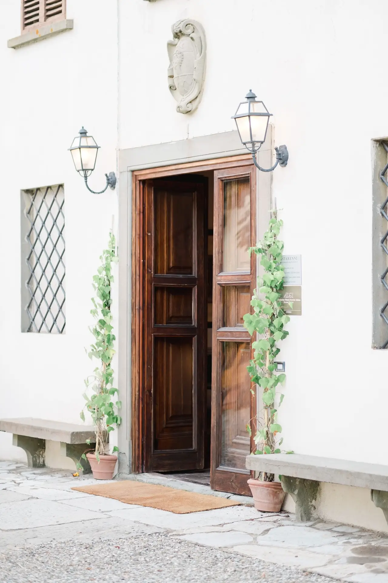 Entrée de la Villa Vistarenni en Toscane avec porte en bois, lanternes murales et plantes en pot, lieu de mariage de charme en Italie.