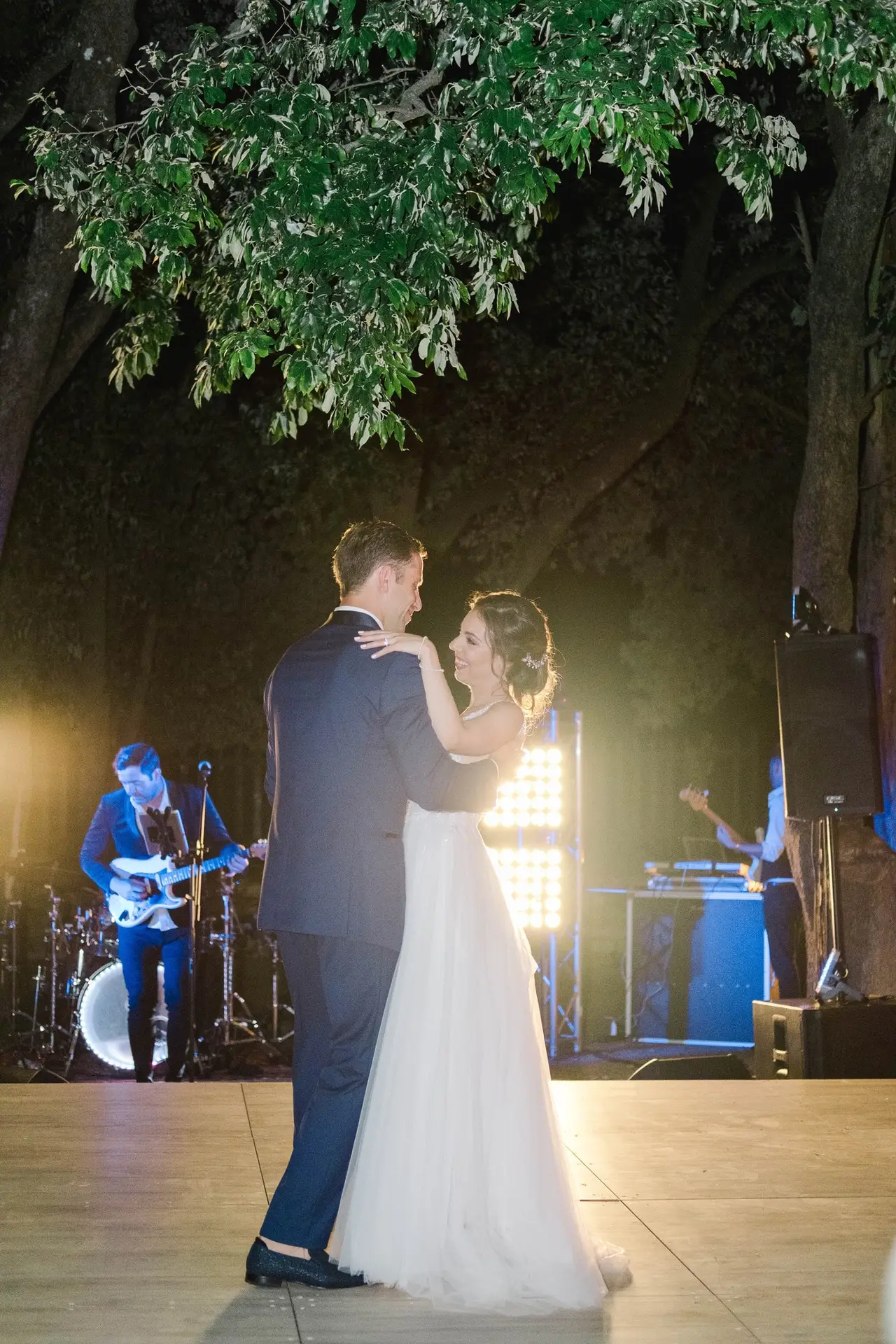 Les mariés dansent leur première danse en extérieur sous les arbres lors de la soirée de mariage à la Villa Vistarenni en Toscane, ambiance musicale live, photo par Julien Boyer.