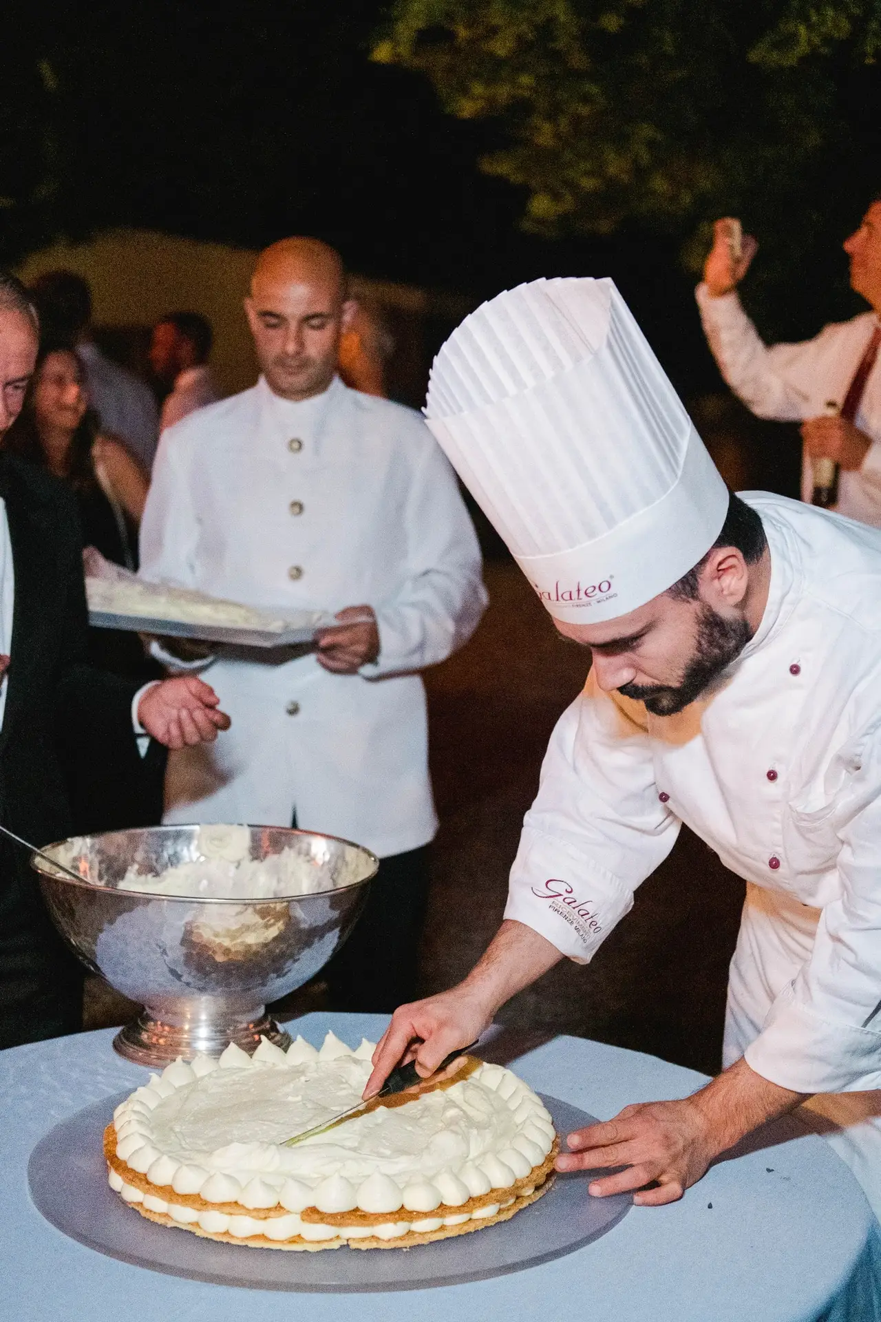 Chef pâtissier découpant le gâteau de mariage lors d’une réception en Toscane, moment gourmand et convivial photographié par Julien Boyer.