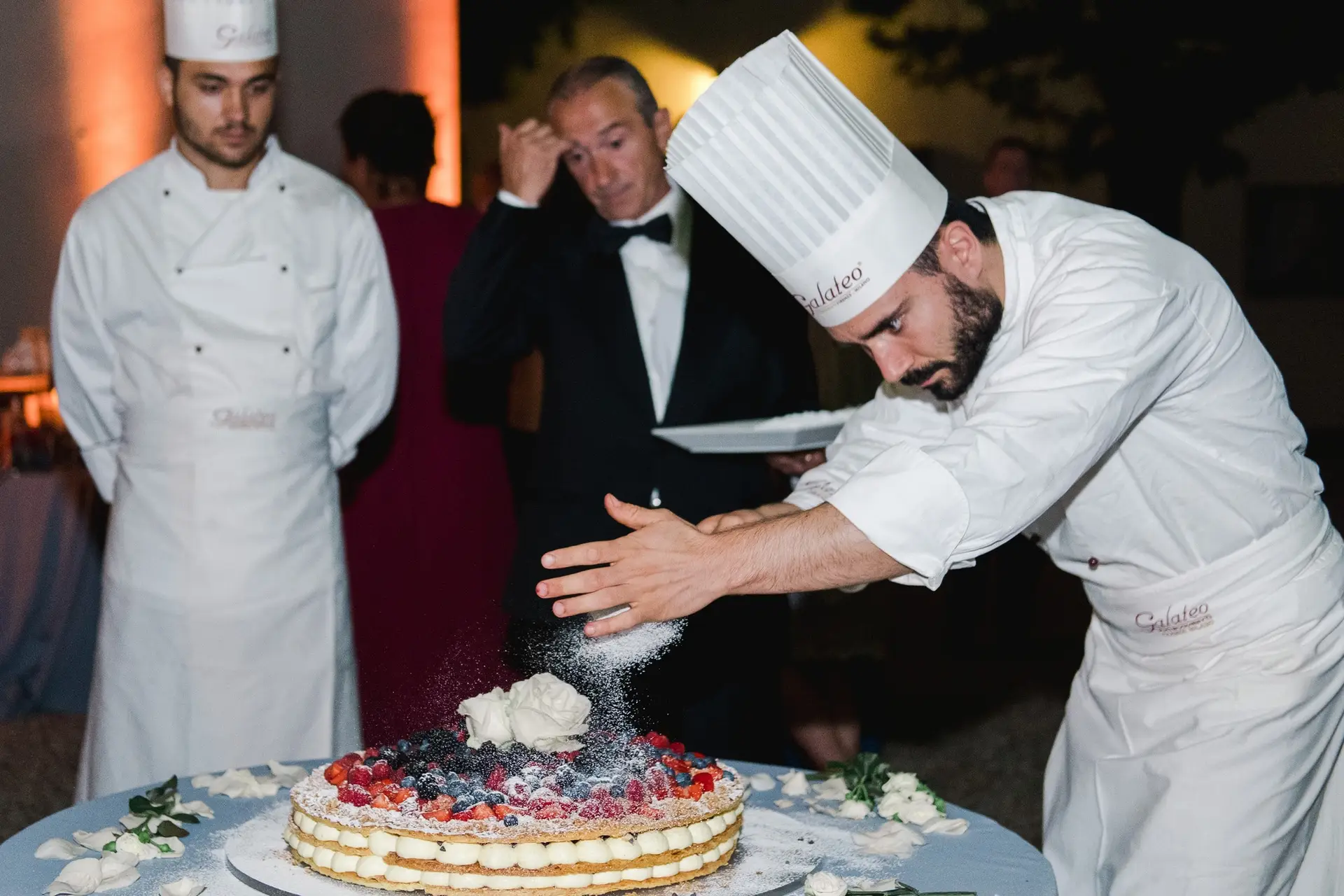 Chef pâtissier finalisant la décoration d’un gâteau de mariage italien aux fruits rouges lors d’un mariage de destination à la Villa Vistarenni.