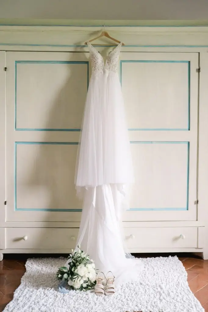 Robe de mariée suspendue dans une chambre de la Villa Vistarenni en Toscane, accompagnée d’un bouquet et de chaussures, photographie de mariage réalisée par Julien Boyer.