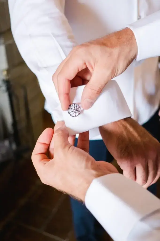 Gros plan sur un bouton de manchette raffiné lors des préparatifs du marié pour un mariage de destination en Toscane.