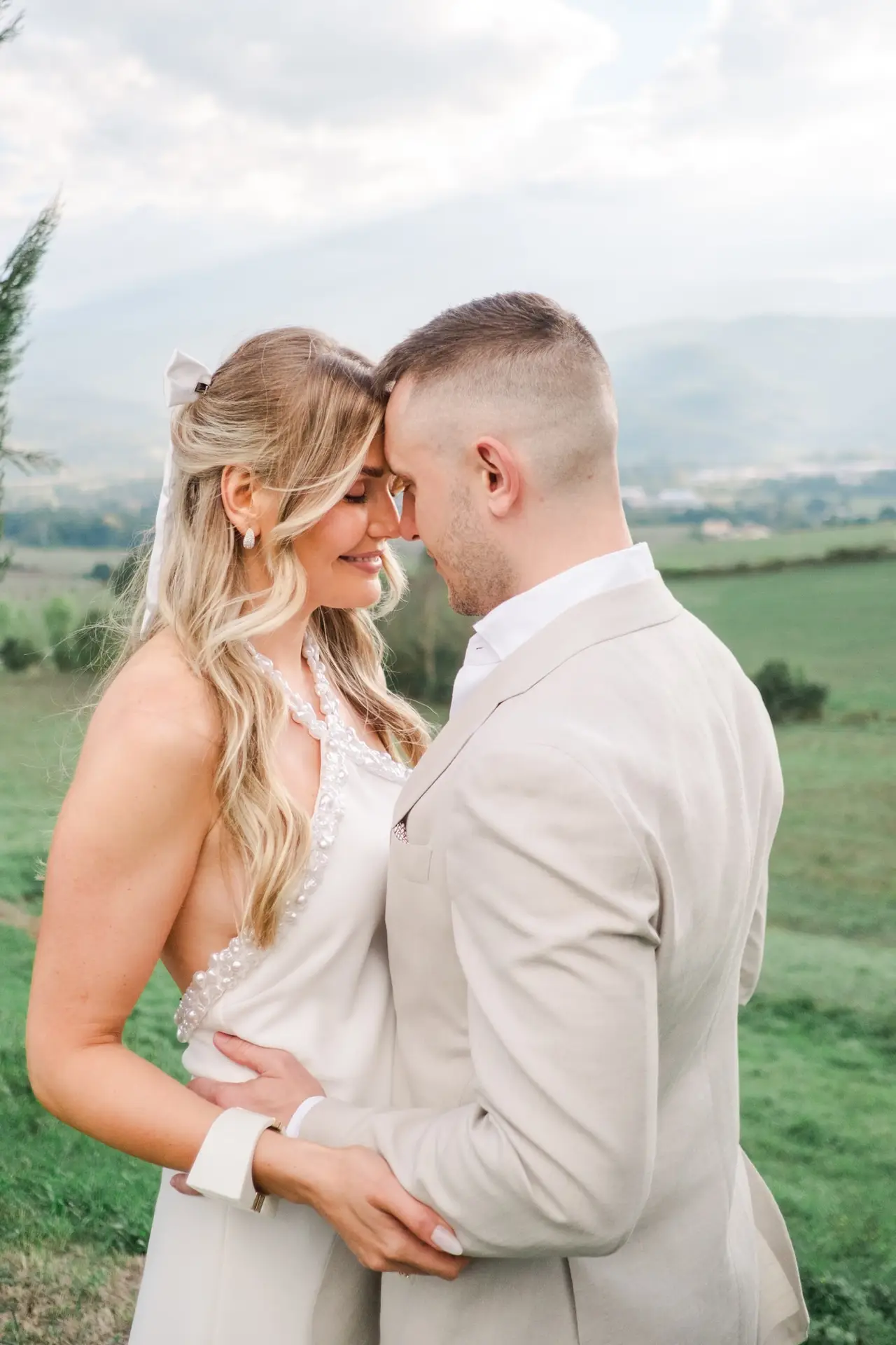 Couple en tenue claire enlacé dans un paysage naturel en Toscane, au Borgo Corsignano, partageant un moment intime photographié par Julien Boyer.