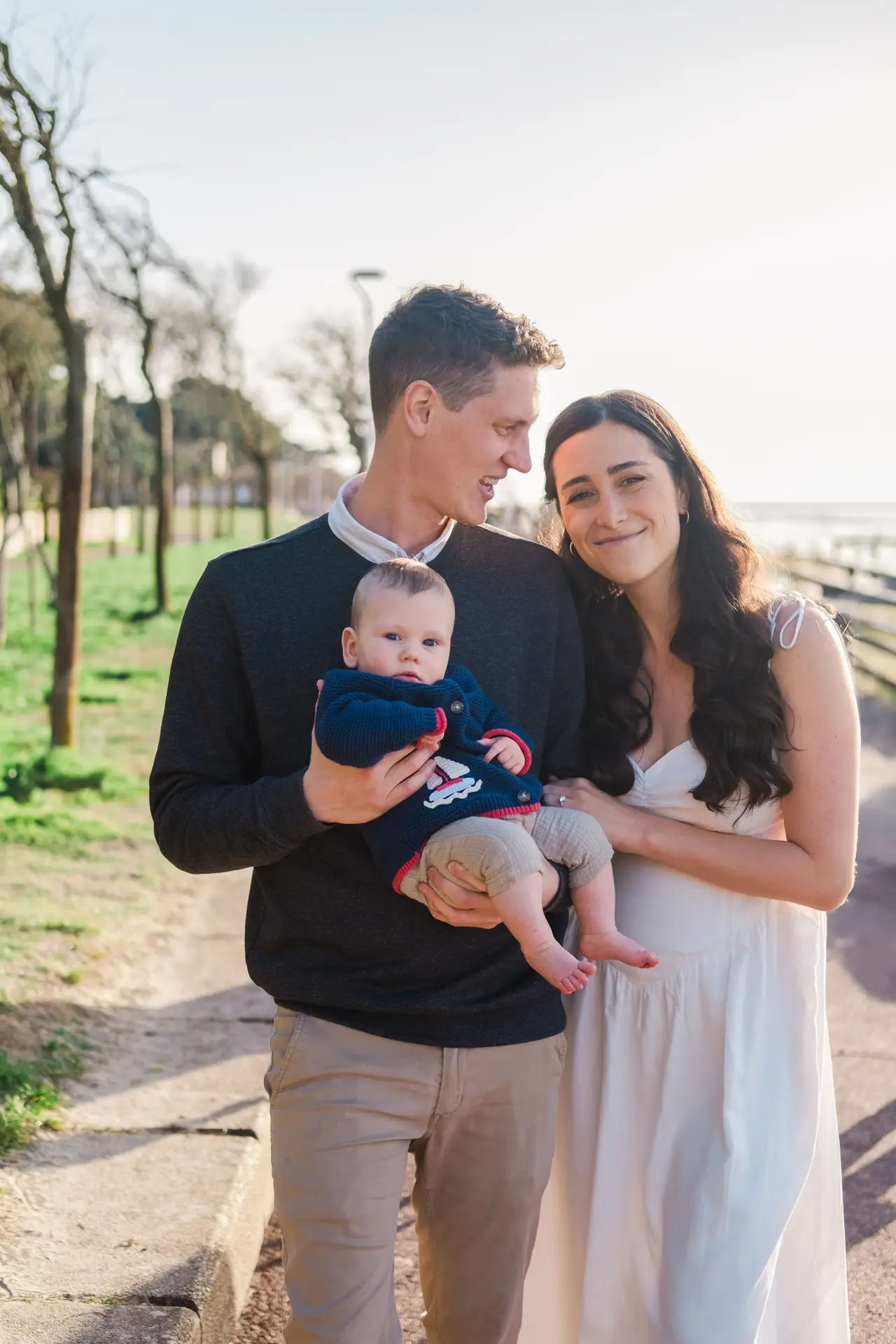 Jeune couple tenant leur bébé dans les bras, portrait de famille en extérieur, ambiance chaleureuse et naturelle.